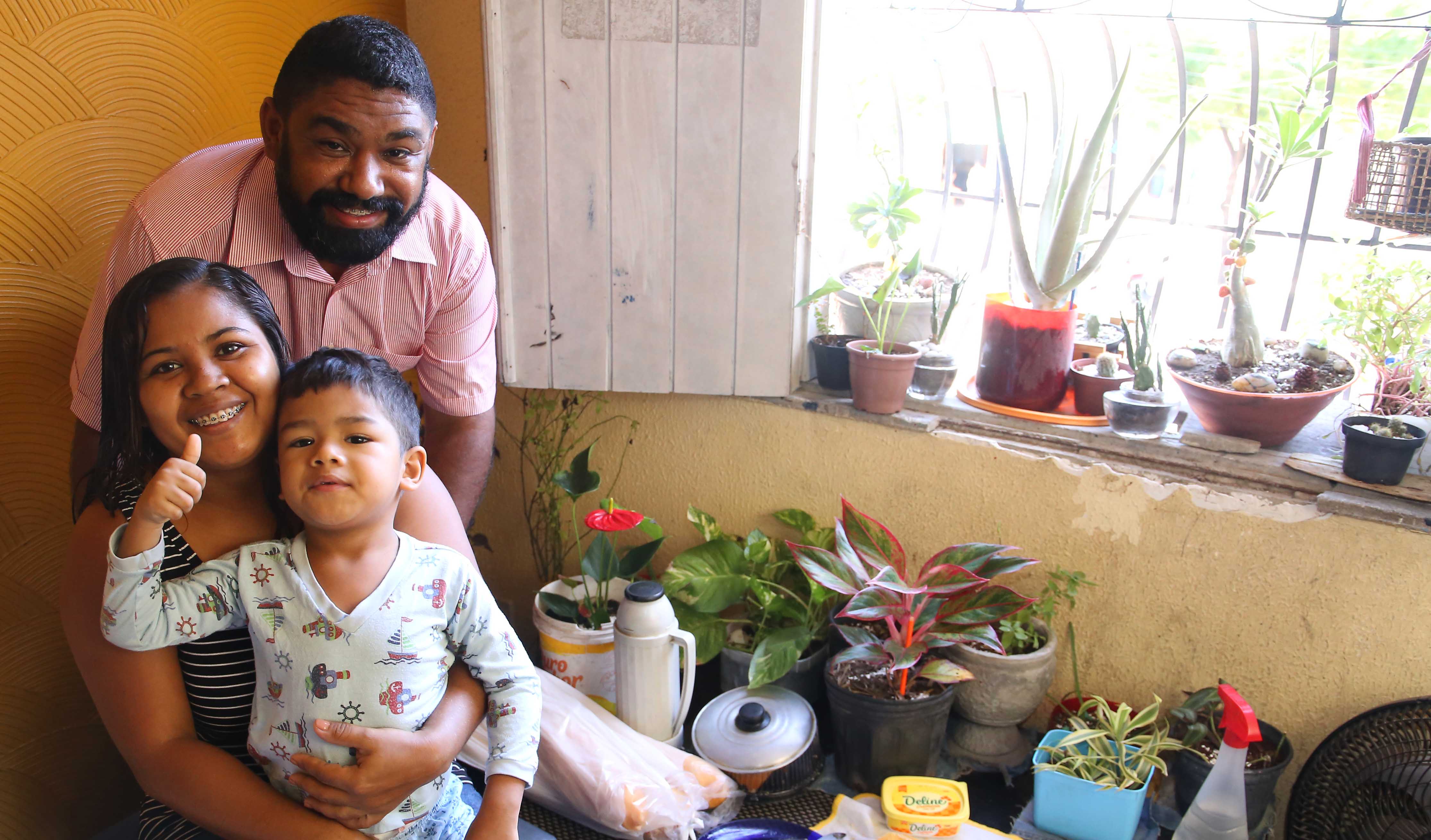 mulher sentada com marido em pé atrás e filho no coloco, todos sorrindo para a foto